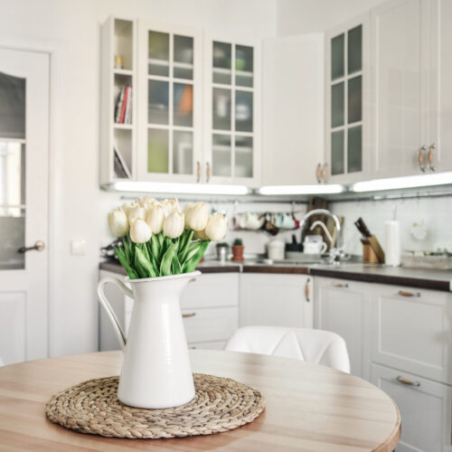 Bouquet of tulips in interior of the kitchen in Scandinavian style with white furniture and a dining table.